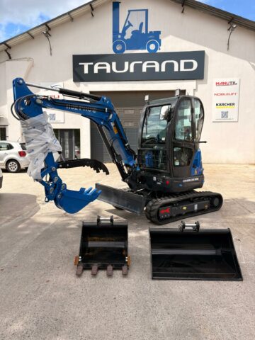 Mini pelle R32 RIPPA avec lame frontale, godets et attache rapide devant le bâtiment Taurand